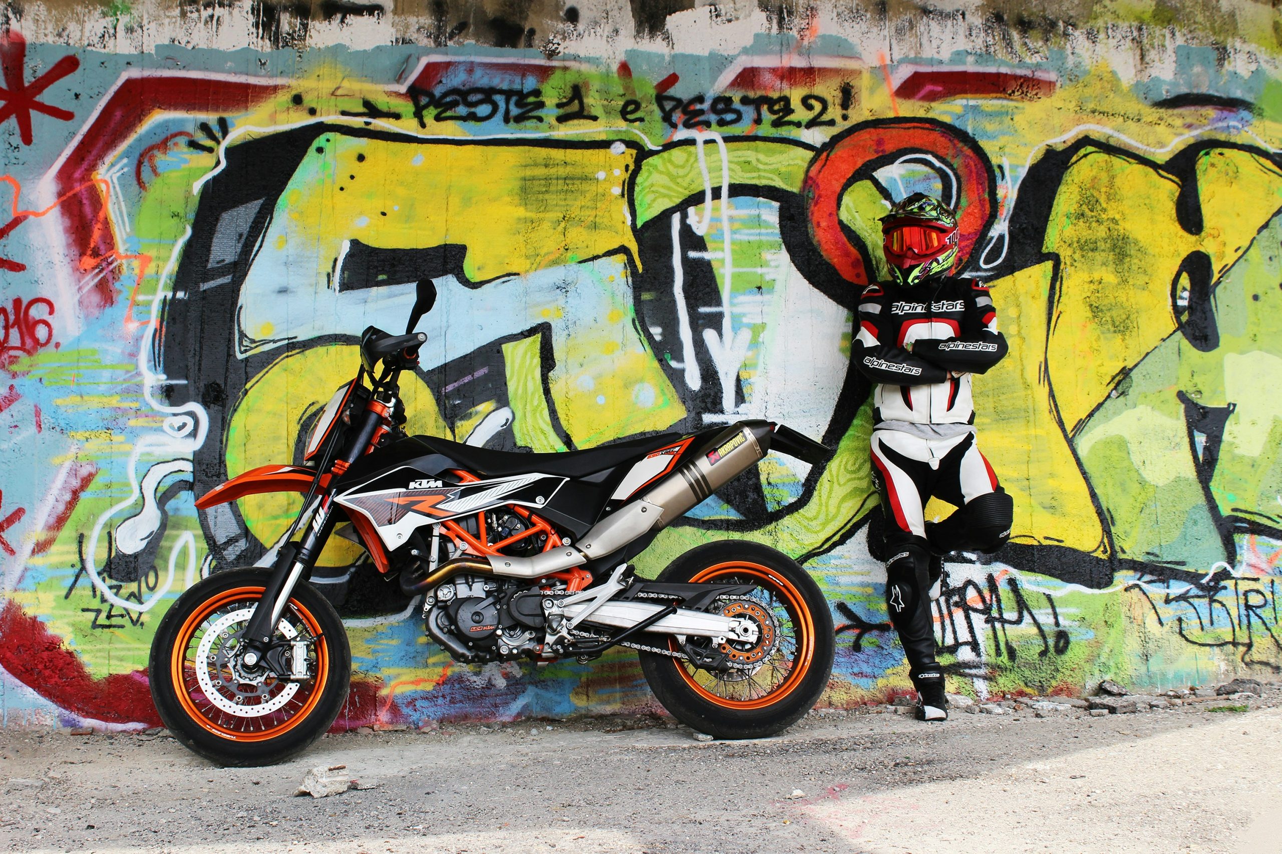 Motorbike and biker on a wall with street art painting.