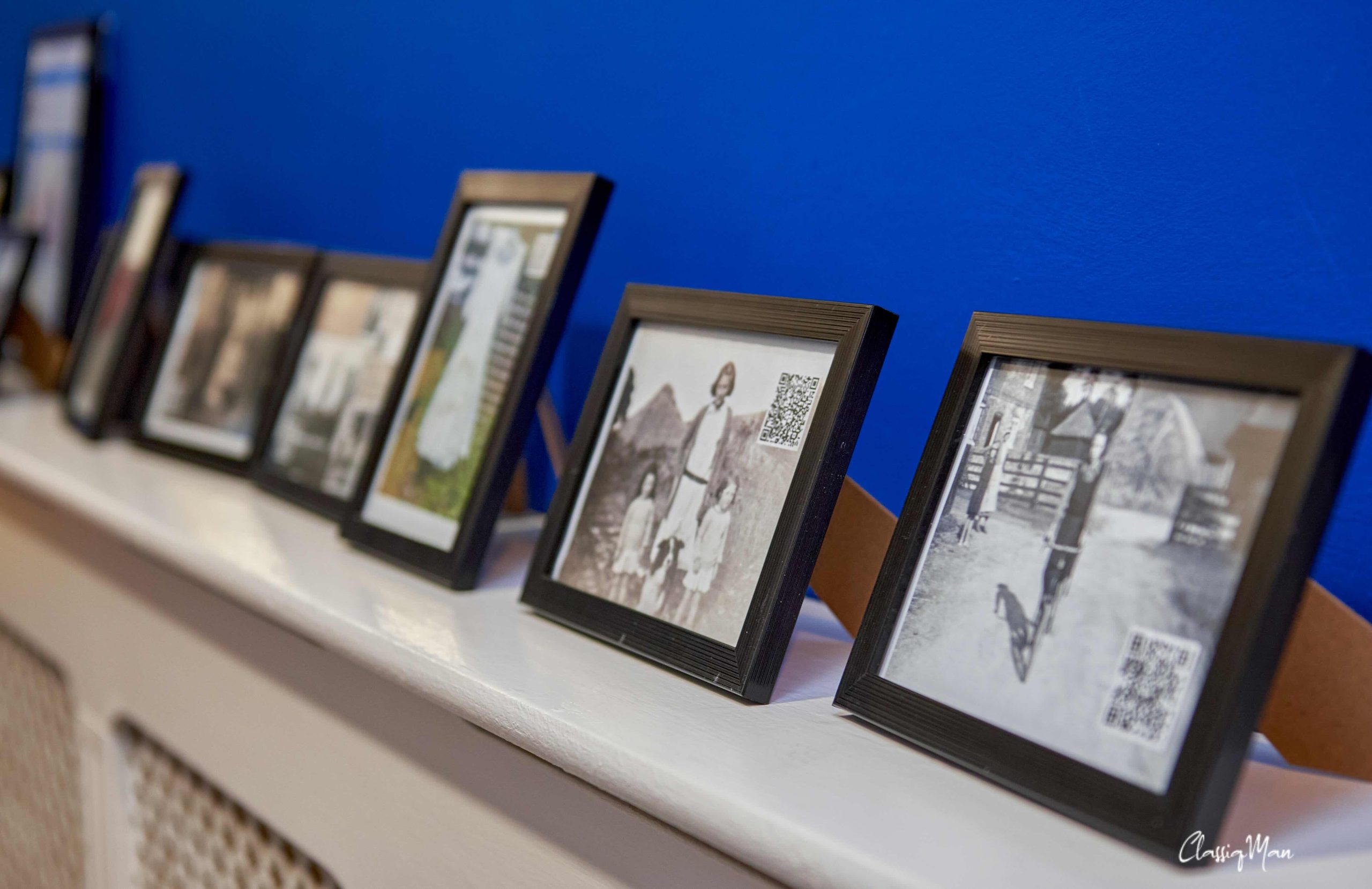 A photo of a shelf which has six vintage photographs in black frames on it.